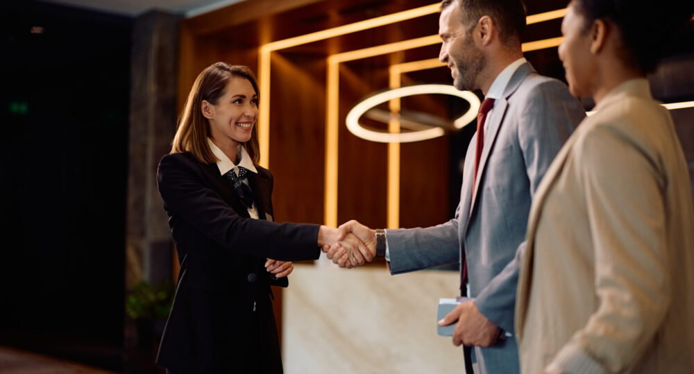 Happy female concierge greeting a business couple in hotel lobby.